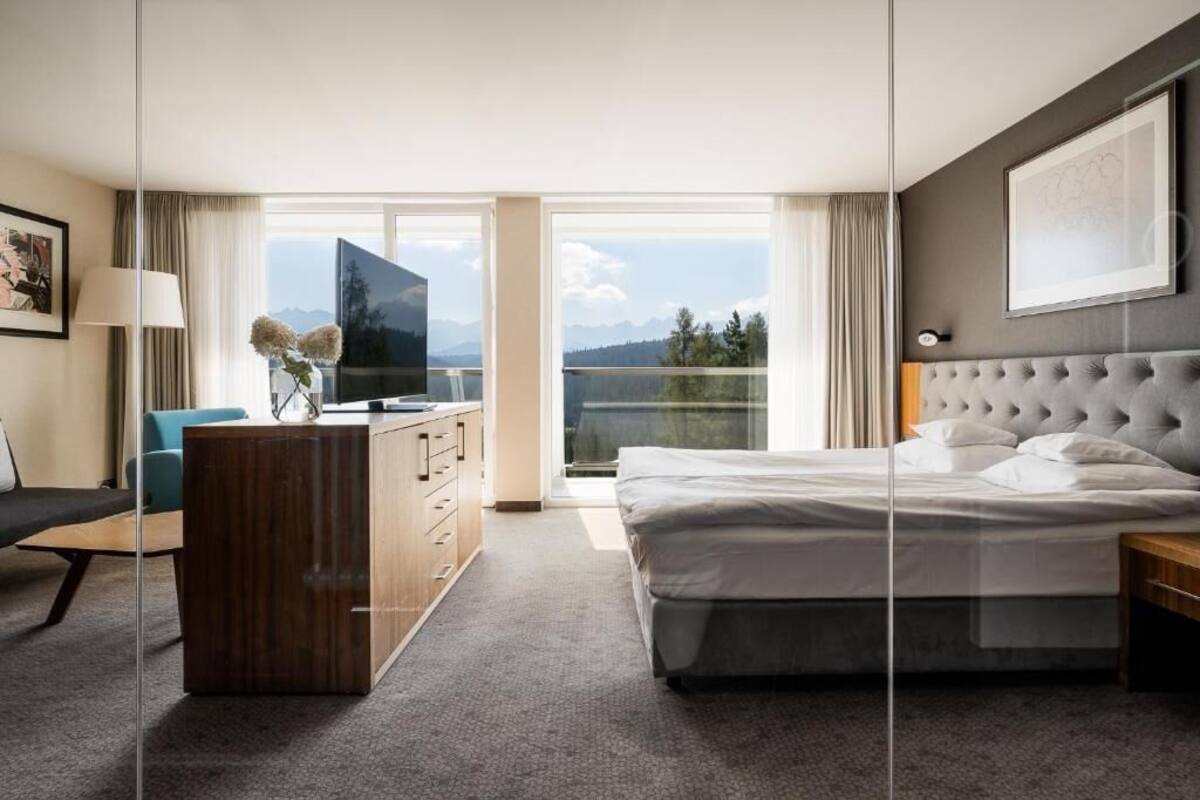 A hotel room with a bed, a desk, a TV, and a view of mountains.