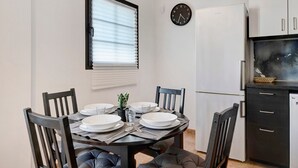 Uma sala de jantar com uma mesa redonda, cadeiras, pratos, talheres, um relógio e uma geladeira.