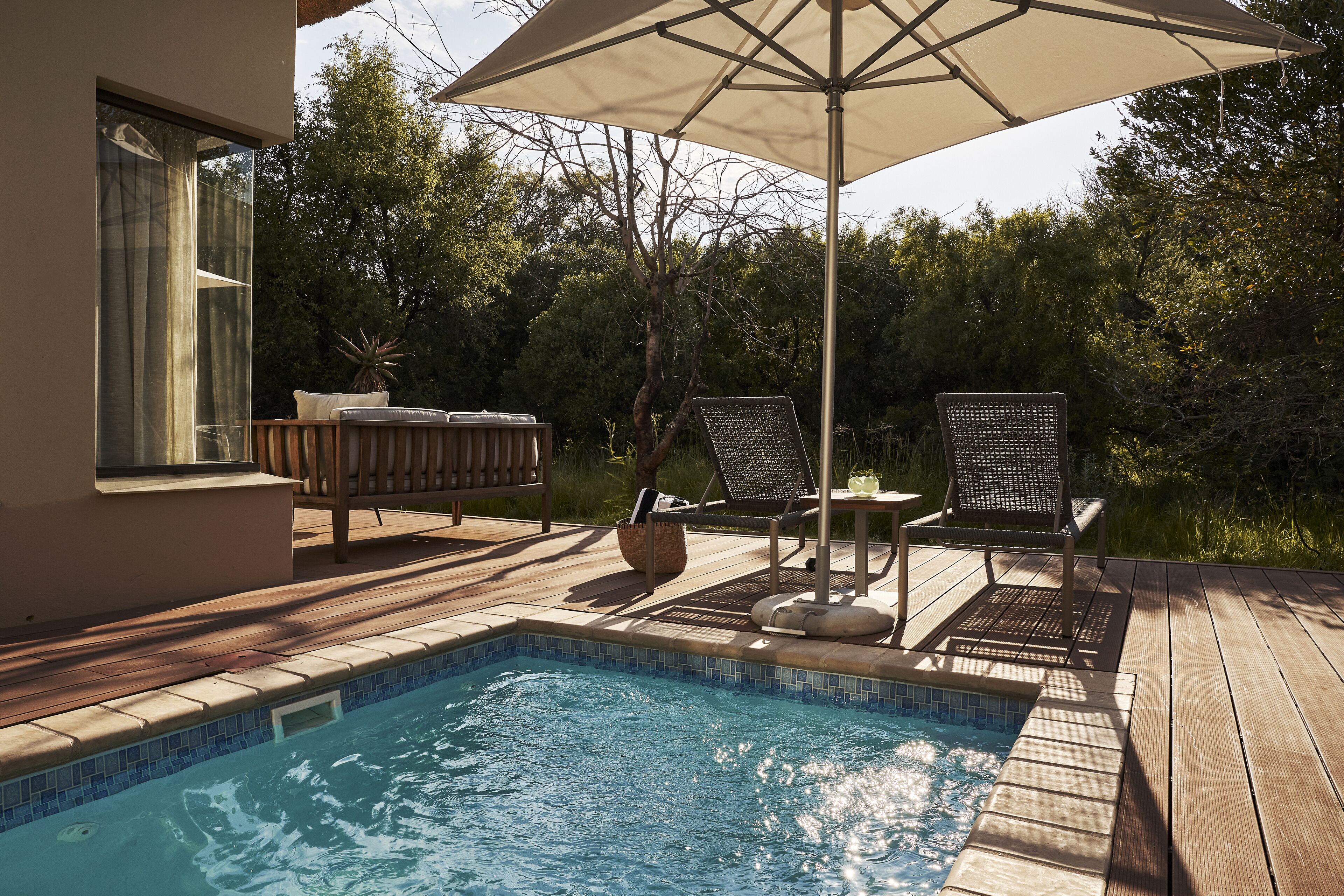 Une piscine avec une terrasse en bois, deux chaises longues et un grand parasol.