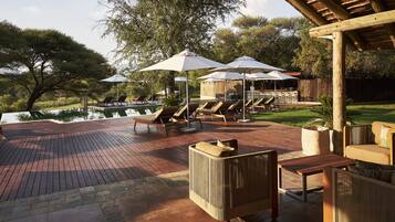 A wooden deck with lounge chairs and umbrellas, overlooking a pool and greenery.