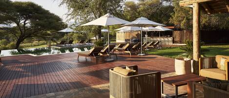 A wooden deck with lounge chairs and umbrellas, overlooking a pool and greenery.