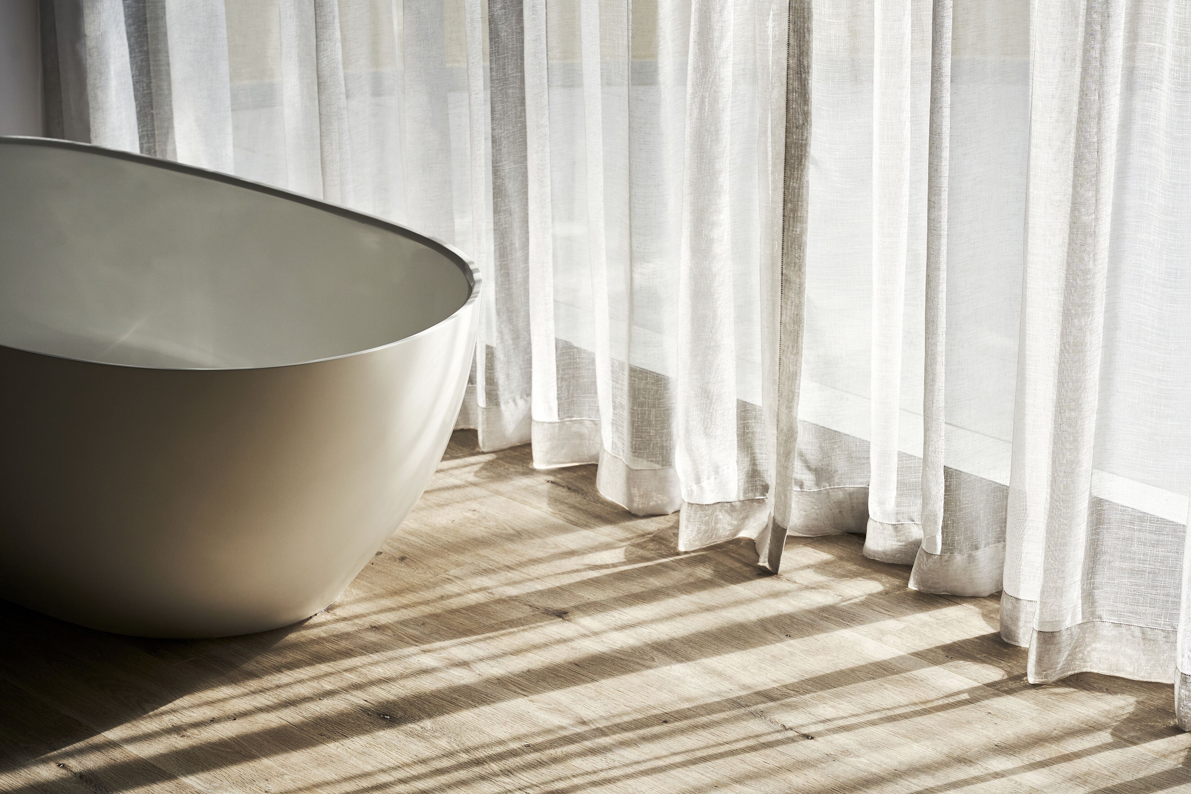 A room with a large, modern, white, bowl-shaped chair near a window with sheer white curtains.