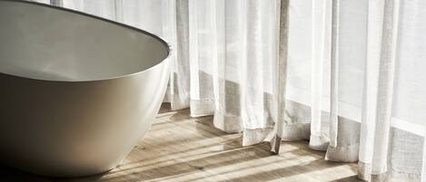 A room with a large, modern, white, bowl-shaped chair near a window with sheer white curtains.