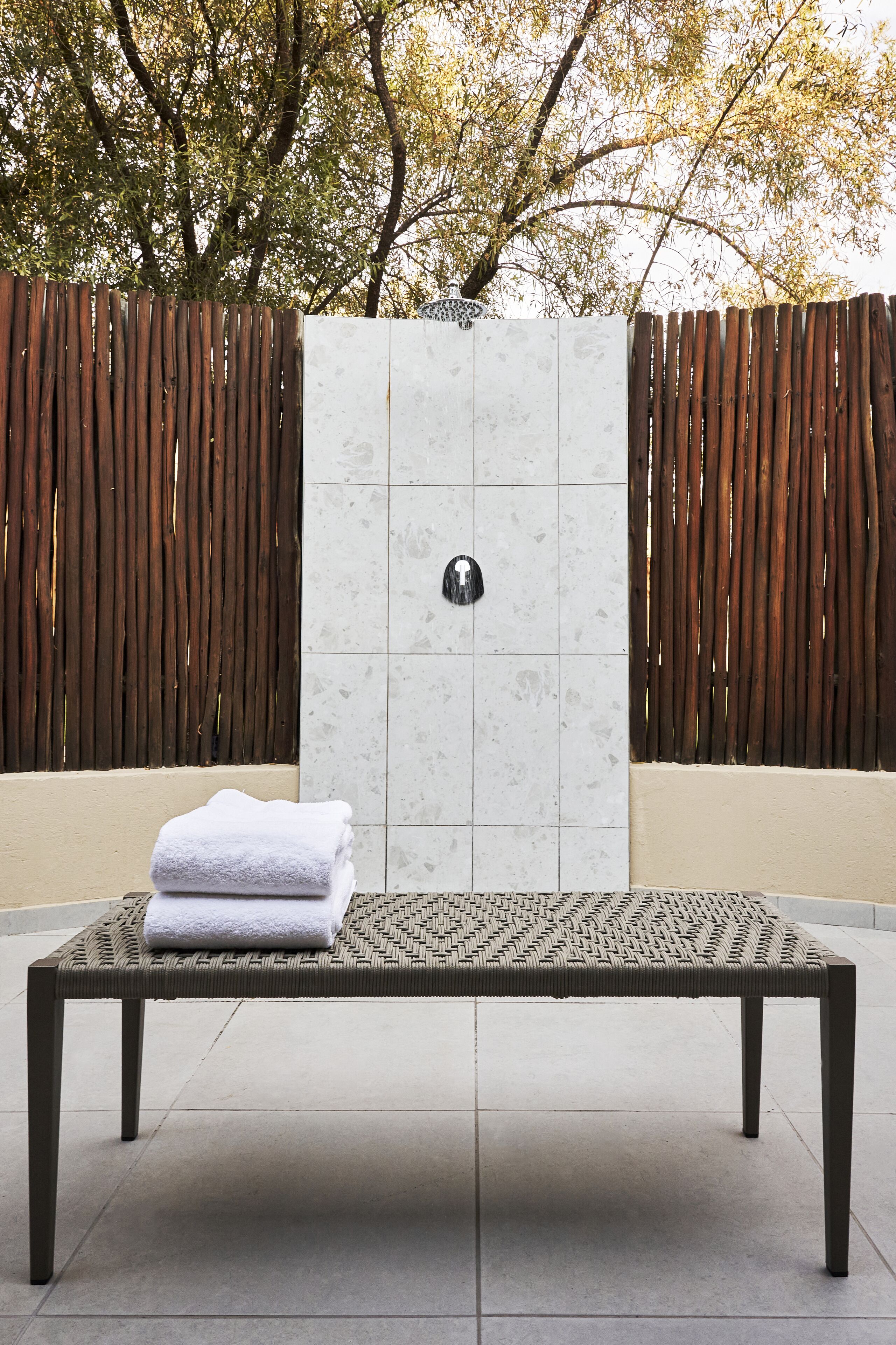A bench with a folded towel in front of a tiled wall with a metallic object.