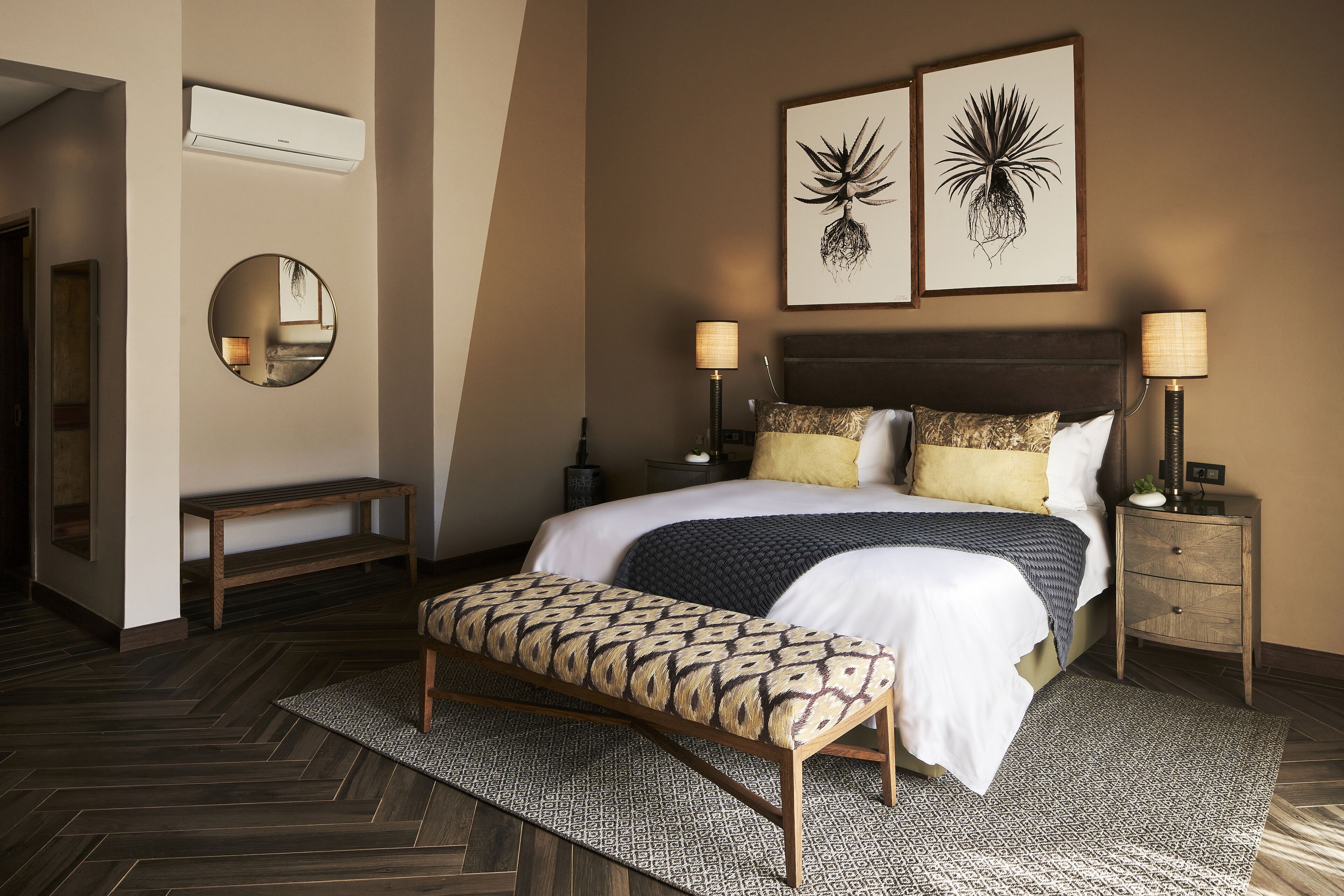 Ein modernes Schlafzimmer mit einem großen Bett, zwei Nachttischen mit Lampen, einem runden Spiegel und zwei an der Wand befestigten Kunstwerken.