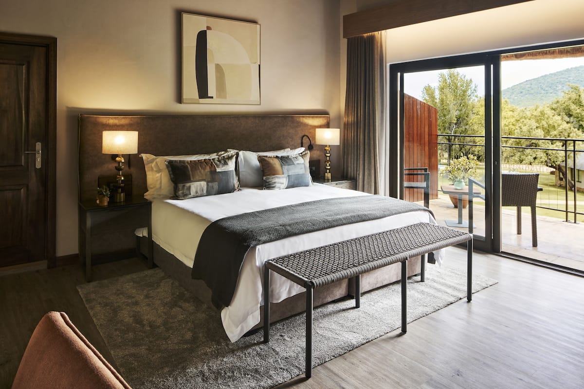 Ein modernes Hotelzimmer mit einem großen Bett, einer Bank, einem Balkon mit Tisch und Stühlen und Blick ins Freie.