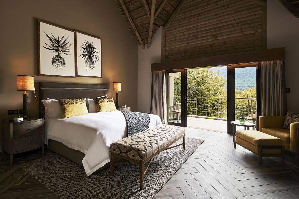 Ein Schlafzimmer mit einem großen Bett, Nachttischen, einer Bank, einem Sofa und einem Balkon mit Blick.