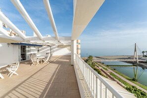 Un balcón con mobiliario exterior, vista al mar y un puente a lo lejos.