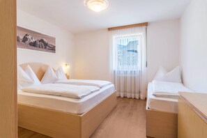 Una habitación de hotel con dos camas, una ventana con cortinas translúcidas, un cuadro colgado en la pared y piso de madera.