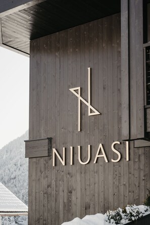 Puinen seinä, jossa on nimi »NIUASI» ja tyylitelty »N»-logo.