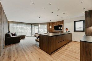 Moderni keittiö, jossa on keskellä sijaitseva saareke, puulattia, upotetut kattovalaisimet ja suuri ikkuna.