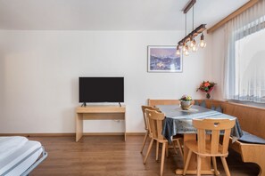 Une chambre moderne dotée d’un bureau en bois, d’un téléviseur à écran plat, d’une table à manger avec des chaises et d’une fenêtre donnant sur un paysage enneigé.