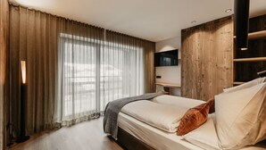 A bedroom with a bed, curtains, a wooden floor, a bedside table, and a wall-mounted TV.