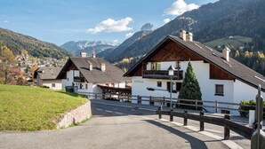 A rural mountain village with traditional wooden houses, a paved road, and a clear view of the surrounding hills.