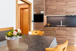 Une table à manger agrémentée d’un centre de table floral, des chaises en bois et une cuisine en arrière-plan.