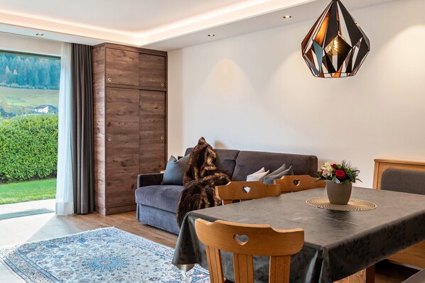 Un salon moderne comprenant un coin repas, une grande fenêtre offrant une belle vue et un luminaire suspendu au design géométrique original.