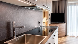 A modern kitchen with a stainless steel sink, a built-in stove, and a flat-screen TV on a wooden cabinet.