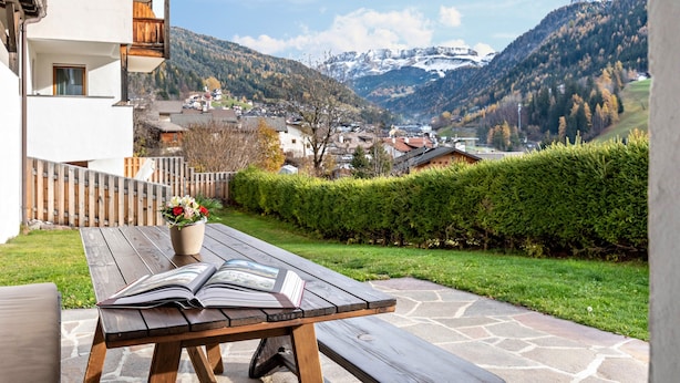 A wooden table with a book and a flower pot on a balcony overlooking a mountainous landscape.