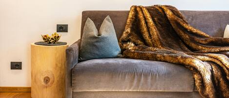 Un sofá gris con un plaid de piel sintética marrón, una almohada azul y una mesita de madera con un cuenco decorativo.