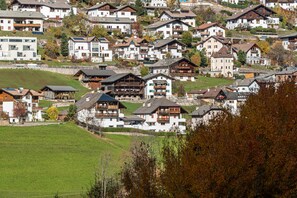 A hillside residential area with multiple houses, some with balconies, and a green field in the foreground.