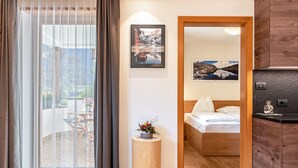 Een hotelkamer met een houten bed, een klein rond tafeltje met een plant, uitzicht door een glazen deur op een buitenruimte, en een schilderij aan de muur.