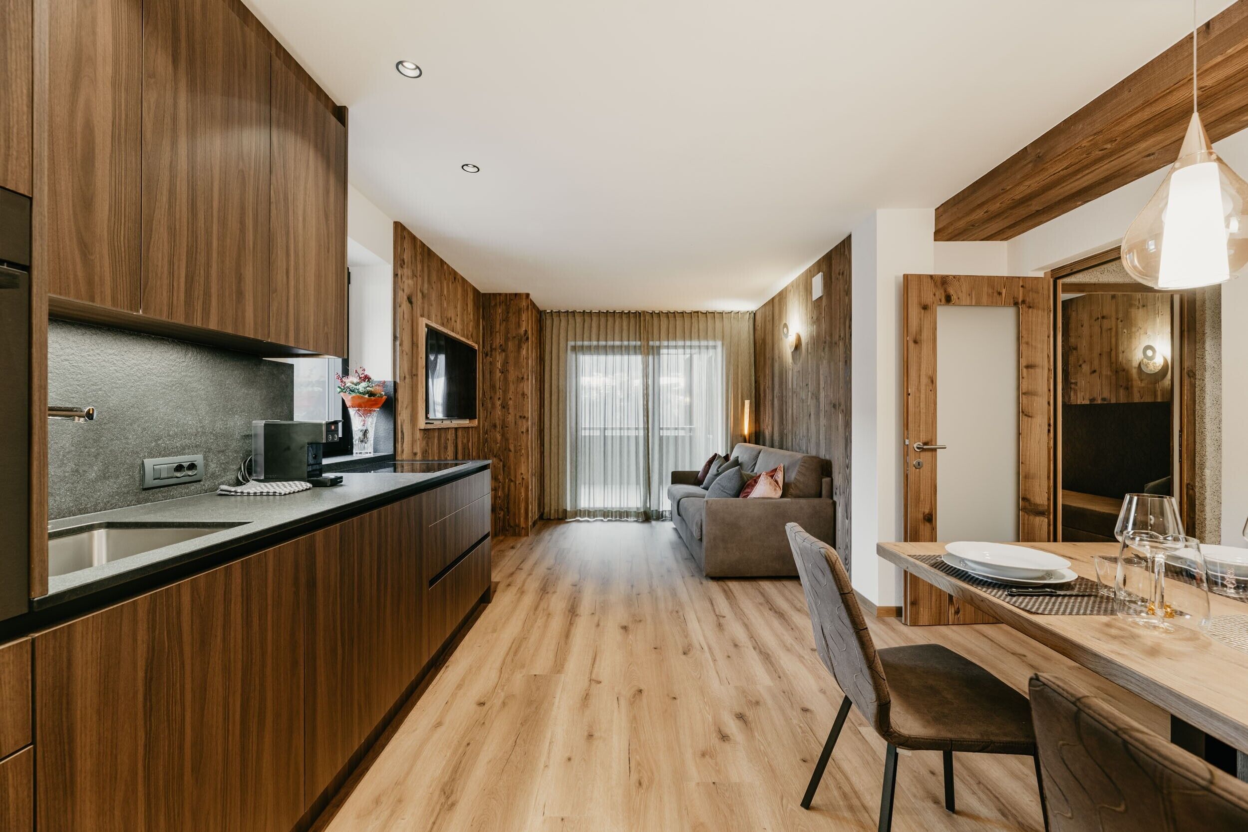 Une cuisine moderne avec des meubles en bois, un coin repas avec une table et des chaises, et un canapé à l’arrière-plan.