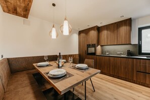 A modern kitchen with wooden cabinets, a dining table set for two, and pendant lighting. - Holiday Apartment "Niuasi" with Mountain View, Terrace and Wi-Fi (Ortisei)
