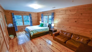 Une chambre dans une cabane en bois, avec un lit, un canapé en cuir et deux fenêtres avec des rideaux.
