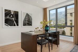 Une pièce moderne avec une grande fenêtre, un bureau en bois et deux chaises noires. Deux tableaux encadrés sont accrochés au mur.