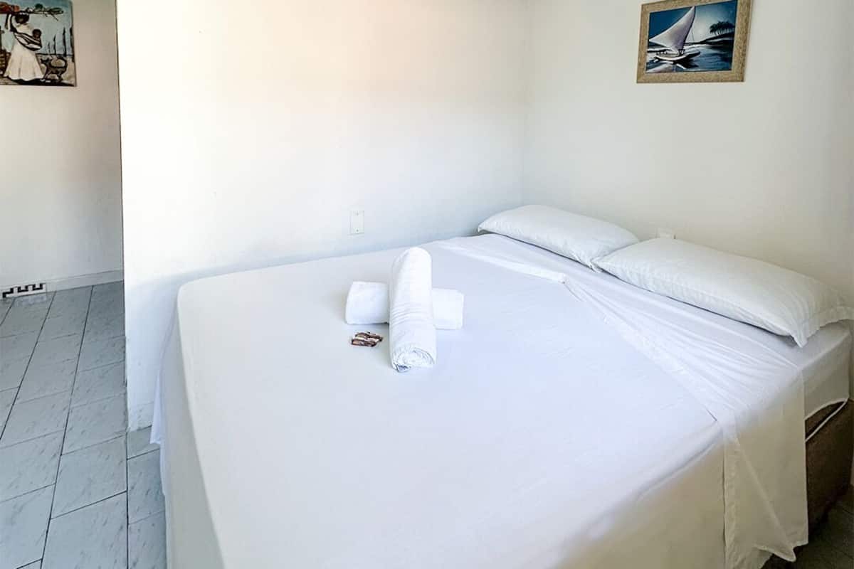 Una habitación limpia y blanca con una cama, un cuadro de un velero y un suelo de baldosas.