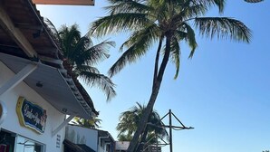 Um hotel na praia com uma placa, palmeiras e vista para o mar.