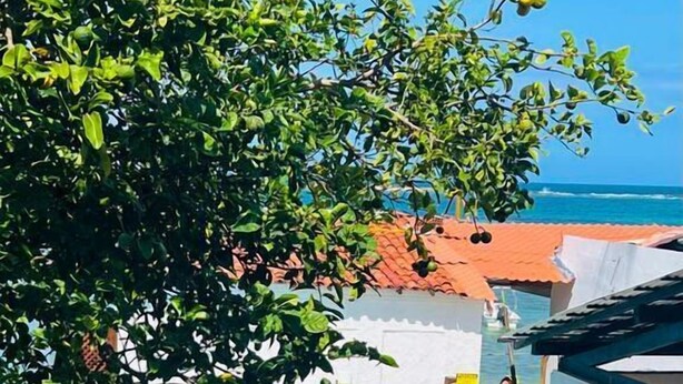 Uma área de piscina com vista clara para o oceano, cercada por um muro branco e um edifício com telhado vermelho.