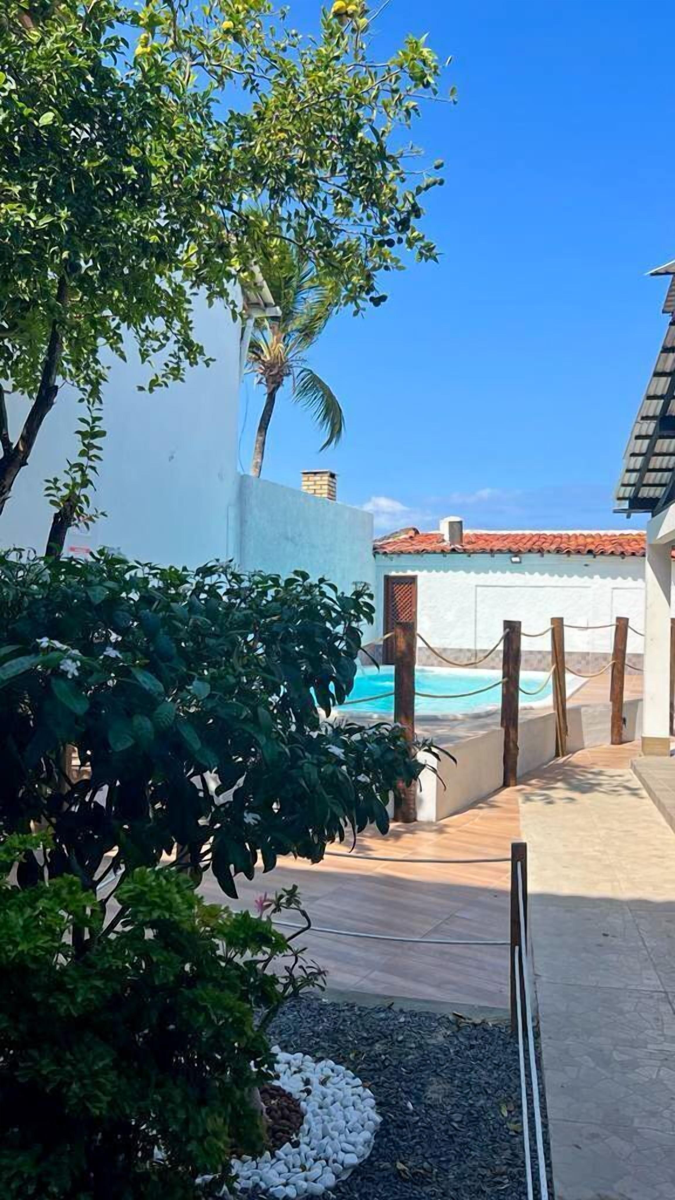Un área de piscina con cielo azul despejado, una palmera y un edificio con techo de tejas.