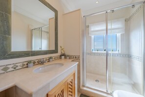 A bathroom with a large mirror, two sinks, a shower with a glass door, and a window with a view. - Villa Bougainvillea (Funchal)