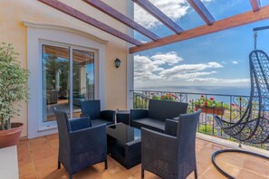 A balcony with wicker furniture, a hanging chair, and a view of the sea. - Villa Bougainvillea (Funchal)