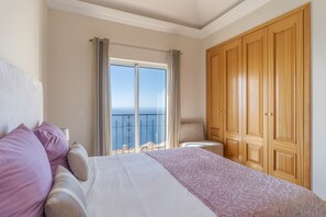 Une chambre à coucher avec un lit, une vue sur la mer et une armoire en bois.