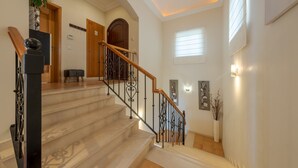 Un escalier doté d’une main courante en bois et de balustrades en métal noir, menant à un palier avec une porte en bois et un petit coin salon.