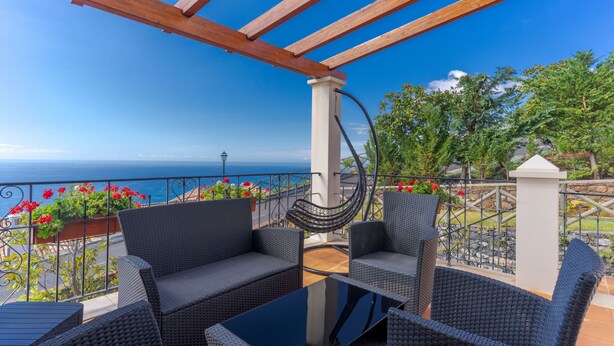 Un balcon doté de meubles en osier et offrant une vue sur la mer.