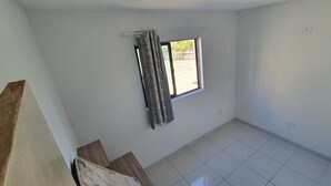 Una habitación con ventana, cortina y suelo de baldosas.