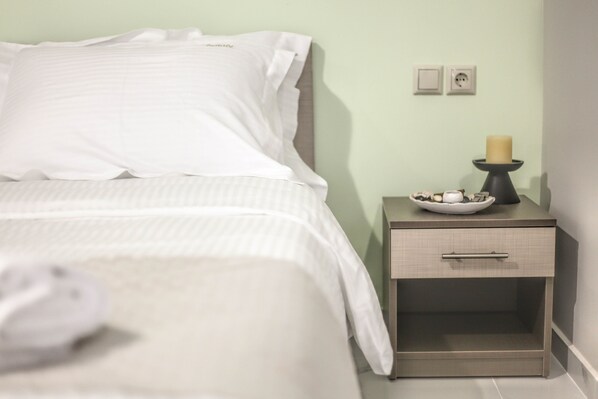 Een opgemaakt bed met witte lakens, een nachtkastje met een kaars en een kleine decoratieve schaal.