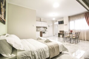 Une chambre avec un lit, une table à manger avec des chaises, un coin cuisine et un téléviseur fixé au mur.