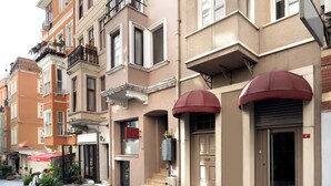 Une rangée d’immeubles à plusieurs étages, dotés de balcons, d’un auvent rouge et d’une porte bien visible avec un numéro.