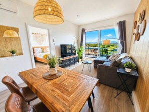 A modern apartment with a dining area, a sofa, a TV, and a balcony with a view.