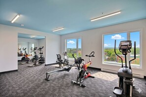 Un gimnasio con diverso equipo de ejercicio, amplias ventanas y suelo alfombrado.