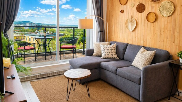 A modern living room with a grey sofa, a small round table, and a view of a balcony with a table and chairs.