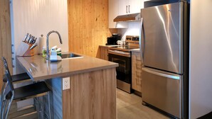 A modern kitchen with a central island, stainless steel appliances, wooden cabinets, and hanging pendant lights.