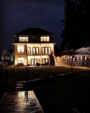 Una casa de dos pisos con un porche iluminado y una entrada protegida por una reja.