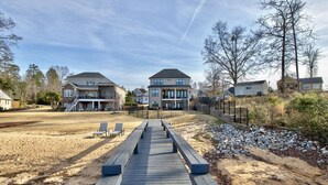 A wooden deck leading to a house with a covered patio and a sandy beach area.