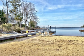 A beach with a wooden dock, chairs, and a house in the background. - Newer Waterfront Lake Murray Home -Dock and Patio -1HR from Masters  (Lexington)