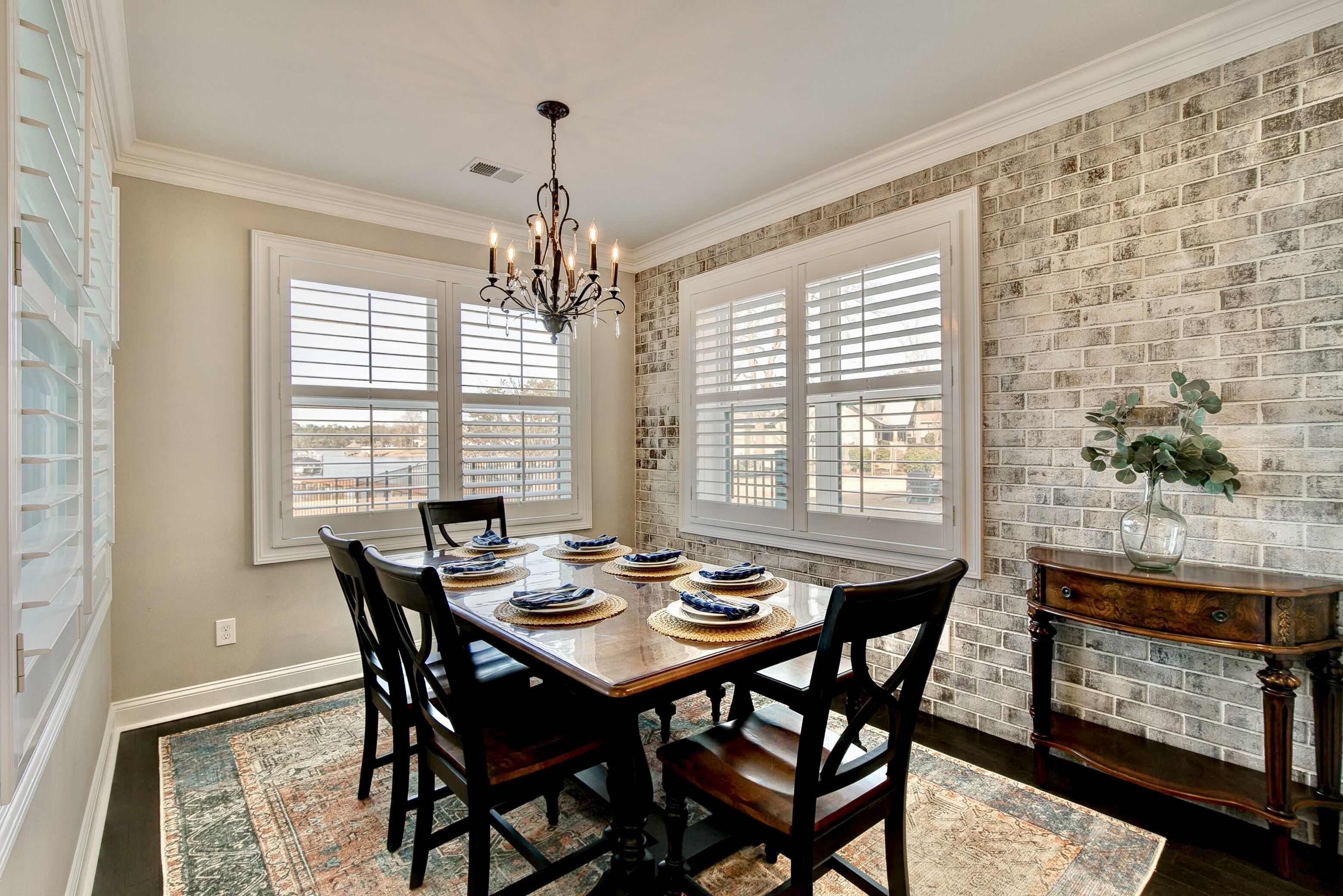 A dining room with a brick wall, large windows, and a chandelier.